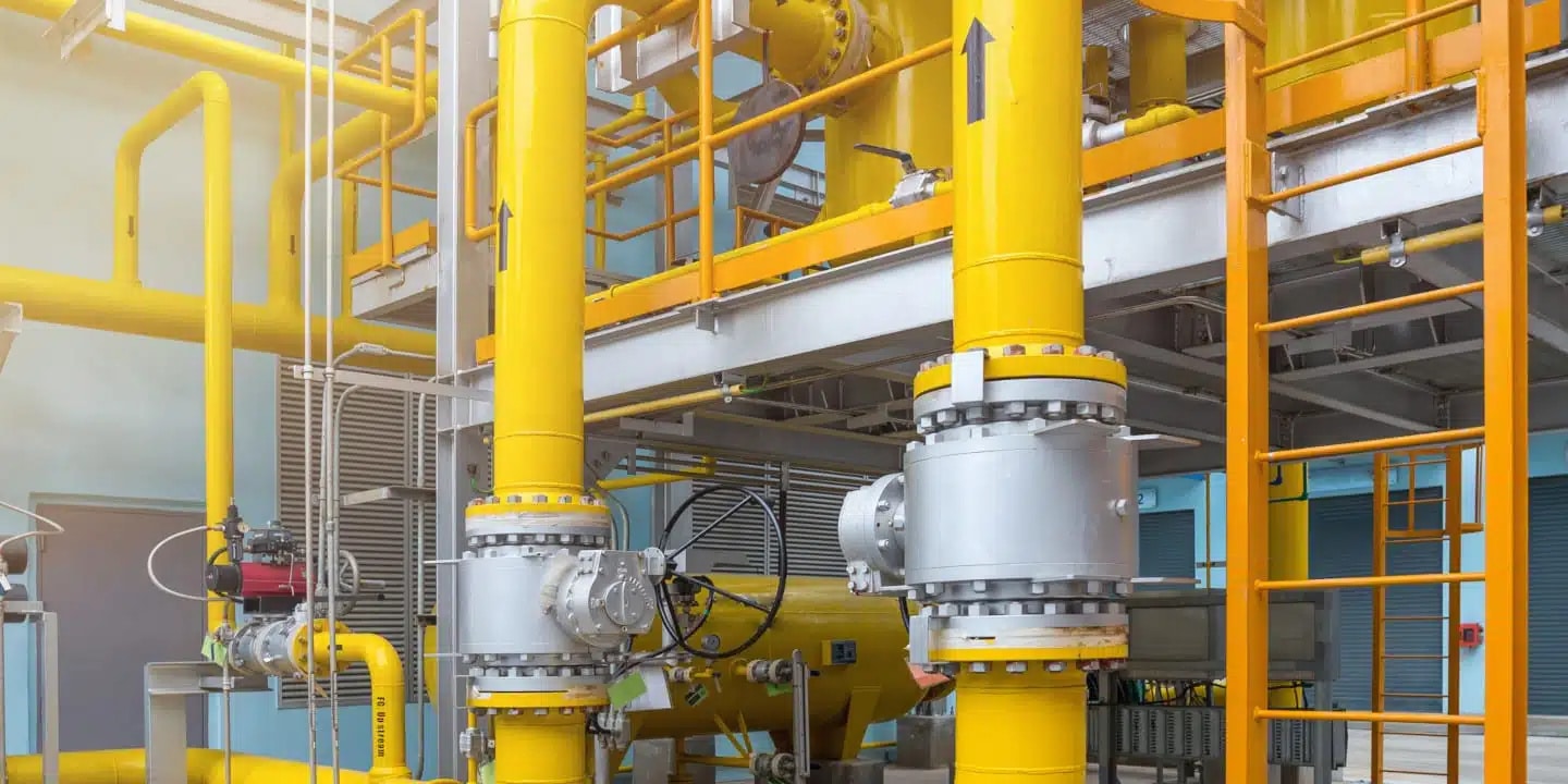 Industrial facility with large yellow pipes, valves, and metal structures, indicating a processing or manufacturing plant environment.