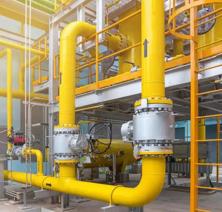 Large yellow industrial gas pipes with metal valves and fittings are installed in a modern facility, featuring multiple levels and structural steel components.