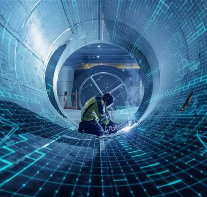 A worker in safety gear welds inside a large metal pipe, with digital blue grid graphics overlaid on the scene.